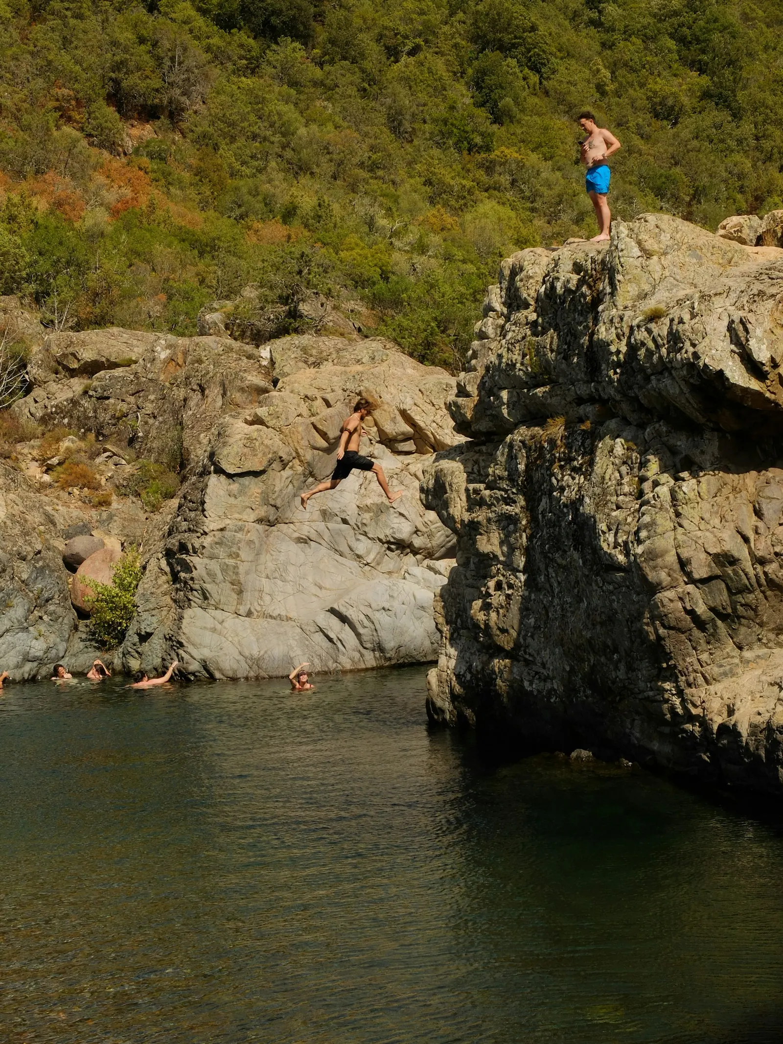 Swimmer jumping from a rock ledge into a river swimming hole